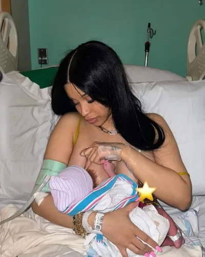 Cardi B shortly after delivering her newborn, lying in a hospital bed, gently holding the baby, both wrapped in blankets, with a peaceful smile.